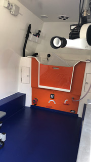 Interior view of a small ambulance featuring a blue floor and medical equipment along the walls.